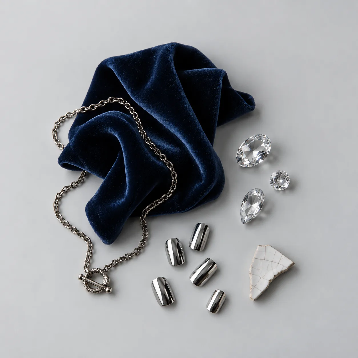 Flat lay of navy velvet, silver chain, crystals and chrome nail tips