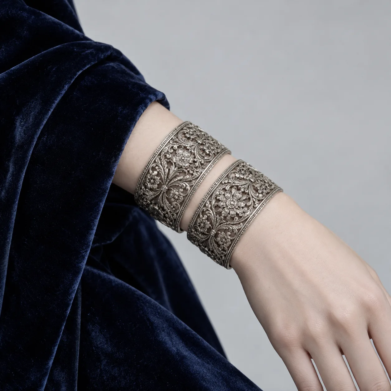 Silver filigree cuffs on a wrist in a navy velvet sleeve